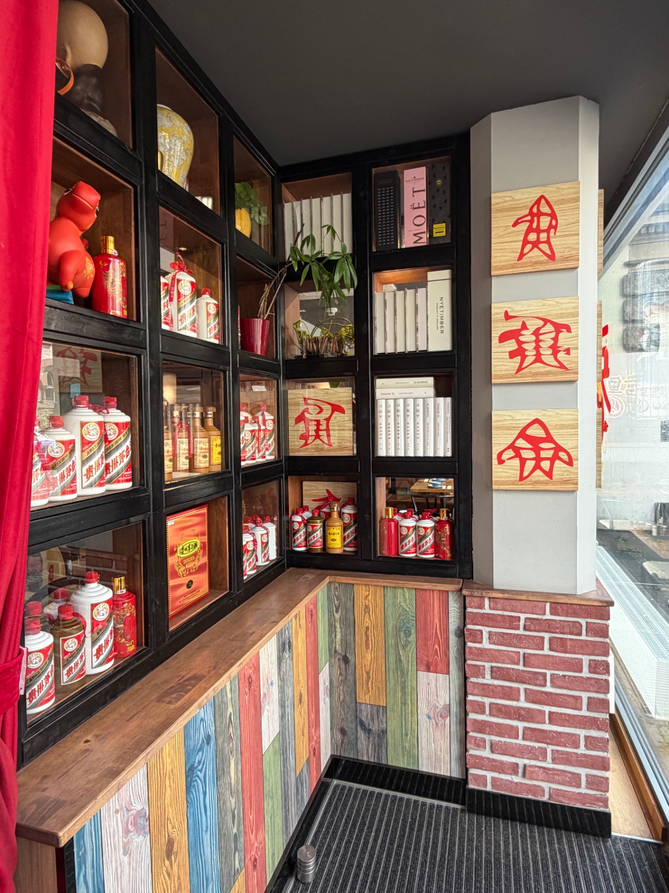 Baijiu-Regal mit Maotai-Flaschen, roten Vorhängen und bunter Holzverkleidung